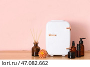 Закрытый маленький косметический холодильник, диффузор и средства по уходу за кожей на столе у розовой стены в комнате. Крупный план. Стоковое фото, фотограф Pixel_shot / Фотобанк Лори