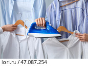 Рука с утюгом и руки, держащие вешалки с одеждой, крупным планом. Стоковое фото, фотограф Pixel_shot / Фотобанк Лори