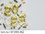 Цифра 2025 из фольгированных шариков с рождественскими украшениями и еловыми ветками на сером фоне. Стоковое фото, фотограф Pixel_shot / Фотобанк Лори