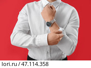 Молодой бизнесмен закатывает рукава на красном фоне, крупным планом. Стоковое фото, фотограф Pixel_shot / Фотобанк Лори