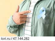 Человек, указывающий на синюю ленту осведомленности на бежевом фоне. Концепция рака простаты. Стоковое фото, фотограф Pixel_shot / Фотобанк Лори