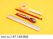 Универсальный нож с клейкой лентой, лезвиями, карандашом и линейкой на желтом фоне. Стоковое фото, фотограф Pixel_shot / Фотобанк Лори