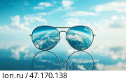 Sunglasses reflecting a vibrant sky and an upside-down view of the earth. Пара солнцезащитных очков сидит на гладкой поверхности, демонстрируя потрясающее отражение голубого неба с облаками и перевернутый вид земли, создавая захватывающую оптическую иллюзию. Стоковое AI-изображение, AI-художник Katsiaryna Repich / Фотобанк Лори