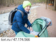 Подросток укрывает одеялом младшего брата в коляске. Старший брат в куртке гуляет с коляской, в которой находится младенец, в парке вдоль замерзшей реки весной. Стоковое фото, фотограф Яна Проничева / Фотобанк Лори