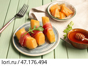 Тарелка с вкусным дыней с прошутто и руколой на зеленом деревянном фоне. Стоковое фото, фотограф Pixel_shot / Фотобанк Лори