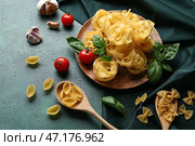 Композиция с различными неприготовленными макаронными изделиями, специями и помидорами на зеленом фоне, крупным планом. Стоковое фото, фотограф Pixel_shot / Фотобанк Лори