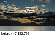 Evening lake landscape. Dark clouds in the blue sky are illuminated with golden light. Silhouettes of coastal hills. Ripples, reflections on the calm surface of the water. Madagascar. Lake Mantasoa. Стоковое фото, фотограф Вера Ивановна Кубарева / Фотобанк Лори