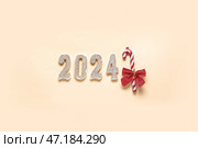 Фигура 2024 с леденцовой тростью и бантом на бежевом фоне. Стоковое фото, фотограф Pixel_shot / Фотобанк Лори