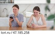 Mother and teen daughter sitting at kitchen table and watching something interesting on their phones. Стоковое видео, видеограф Яков Филимонов / Фотобанк Лори