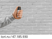 Молодой человек с перцовым баллончиком для самообороны на фоне серого кирпича, крупным планом. Стоковое фото, фотограф Pixel_shot / Фотобанк Лори