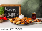 Доска с текстом HAPPY NOWRUZ, трава, угощения, свеча и стакан чая на столе возле гранж-стены. Стоковое фото, фотограф Pixel_shot / Фотобанк Лори