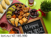 Доска с текстом HAPPY NOWRUZ, угощения, стакан чая и травы на зеленом фоне. Стоковое фото, фотограф Pixel_shot / Фотобанк Лори