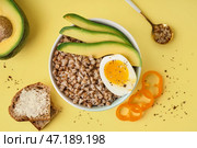 Тарелка вкусной гречневой каши с яйцом всмятку, свежими овощами и хлебом на желтом фоне. Стоковое фото, фотограф Pixel_shot / Фотобанк Лори