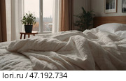 The interior of a modern house. A minimalistic cozy beige bedroom interior with a plaid, pillows, a headboard, linen linens and a bedside table. Стоковое AI-изображение, AI-художник Photojuli / Фотобанк Лори