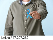 Человек с голубой лентой на цветном фоне, крупным планом. Концепция рака простаты. Стоковое фото, фотограф Pixel_shot / Фотобанк Лори