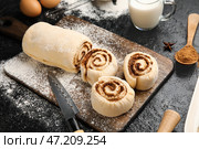 Деревянная доска с сырыми булочками с корицей на черном фоне. Стоковое фото, фотограф Pixel_shot / Фотобанк Лори
