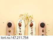 Вкусные глазированные эклеры и цветочный декор на бежевом фоне. Стоковое фото, фотограф Pixel_shot / Фотобанк Лори