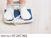 Тощая женщина с измерительной лентой, стоящей на напольных весах. Понятие анорексии. Стоковое фото, фотограф Pixel_shot / Фотобанк Лори