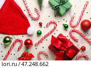 Композиция со сладкими карамельными тростями, рождественскими подарками, шарами и шапкой Санты на светлом фоне. Стоковое фото, фотограф Pixel_shot / Фотобанк Лори