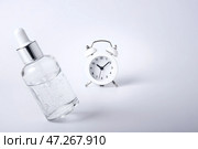 Bottle of face serum levitates on a white background next to the retro alarm clock. Стоковое фото, фотограф София Тюленева / Фотобанк Лори
