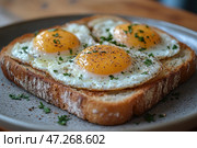 A delicious breakfast – three sunny-side-up eggs served on a toasted slice of bread. The yolks are bright golden, slightly shiny, the whites are tender and gently cooked. The dish is sprinkled with fresh herbs, probably parsley or dill, and seasoned with ground black pepper. The bread is crispy, with a golden crust and soft crumb. All this is served on a ceramic plate, creating the feeling of a homey, cozy breakfast. Стоковое AI-изображение, AI-художник Анна Кривицкая / Фотобанк Лори