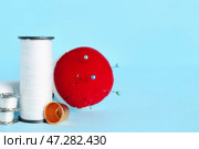 Катушки с белыми нитками, наперсток и подушечка для иголок с булавками на цветном фоне. Стоковое фото, фотограф Pixel_shot / Фотобанк Лори