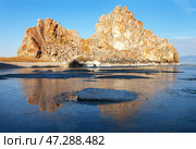 Spring morning on Baikal Lake. View of the famous Shamanka rock - a natural landmark of Olkhon Island in the rays of the rising sun. The bay is covered with a thin crust of blue ice. Scenic spring landscape. Стоковое фото, фотограф Виктория Катьянова / Фотобанк Лори