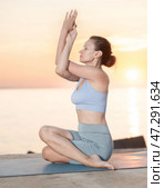 Young woman maintaining mental and physical health attending, practicing twisting yoga exercises on beach at morning. Стоковое фото, фотограф Яков Филимонов / Фотобанк Лори
