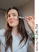Home lymphatic drainage facial massage with a metal roller: woman refreshes skin, making it firm and smooth. Стоковое фото, фотограф Svetlana Golovco / Фотобанк Лори