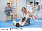 Pair of teenager boys practicing new self-defense moves during training in gym, learning painful pronating wristlock on opponent lying face down on floor. Стоковое фото, фотограф Яков Филимонов / Фотобанк Лори