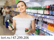 Cheerful Asian woman examining bottles of soju in store. Стоковое фото, фотограф Яков Филимонов / Фотобанк Лори