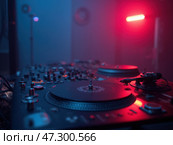 A Close-Up of a DJ\'s Turntables Illuminated by Vibrant Blue and Red Lights During a Nighttime Session at a Local Venue. Стоковое AI-изображение, AI-художник Sergey Grishin / Фотобанк Лори