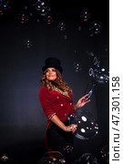 A skilled woman magician dons a theatrical outfit while enchantingly showcasing her soap bubble performance. Her playful smile and intricate bubble formations create a mesmerizing atmosphere. Стоковое фото, фотограф Aleksandr Golubev / Фотобанк Лори