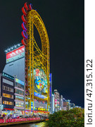 Osaka, Japan - Sep 22 2024, panoramic view from below of Don Quijote Dotonbori shopping and entertainment complex and Ferris wheel, in Dotonbori district, on canal corniche, at nighttime, Osaka, Japan. Редакционное фото, фотограф Сергей Богомяко / Фотобанк Лори