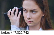 Young schoolgirl wearing headphones, listening intently to voice message on smartphone while sitting alone in green park setting. Стоковое фото, фотограф Mikhail Davidovich / Фотобанк Лори
