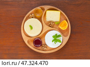 Cheese plate with three kinds of cream cheeses with basil, mandarin, honey, fruit jam and walnuts on a round tray on a wooden table. Healthy organic nutritious food. Flat lay, top view, copy space. Стоковое фото, фотограф Виктория Катьянова / Фотобанк Лори