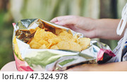 Woman relaxing outdoors, munching crispy potato chips, savoring salty treat during bright afternoon sunlight. Стоковое фото, фотограф Mikhail Davidovich / Фотобанк Лори
