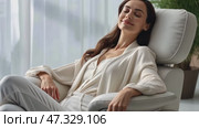 Happy millennial Caucasian woman sit in cozy chair in design home stretch relax breathe fresh air. Smiling young female renter or tenant rest in armchair relieve negative emotions enjoying weekend. Стоковое AI-видео, аниматор Sergey Grishin / Фотобанк Лори