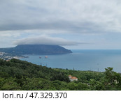 A picturesque view of Gurzuf from above. In the center of the composition is the majestic Mount Ayu-Dag, covered with a thick cap of clouds, like a magic veil. Below is the coast with houses, hotels and a bay in which the famous Adalary rocks are visible, like two guards at the entrance to the sea. Everything is surrounded by dense Crimean forests and greenery, creating a feeling of silence, peace and harmony. The atmosphere is filled with cool freshness, the breath of the sea and the anticipation of something new. Стоковое фото, фотограф Анна Кривицкая / Фотобанк Лори