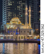 UAE, Dubai, 10 December 2024: Mosque of Muhammad Ibn Ahmad Al-Mullah against the backdrop of skyscrapers at night in Dubai Marina, yachts sailing by, reflection of night lighting on the water. Редакционное фото, фотограф Vladimir Drozdin / Фотобанк Лори