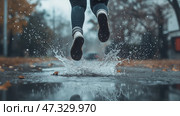 Runner splashes through puddles on a rainy day in the city. Человек бежит трусцой по городской улице, плескаясь в лужах, образовавшихся после недавнего дождя. Яркие осенние листья окружают дорожку, усиливая сезонное очарование сцены. Стоковое AI-изображение, AI-художник Katsiaryna Repich / Фотобанк Лори