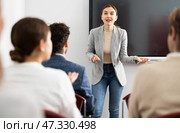 Positive skilled female coach explaining topic to group of people during foreign language class in auditory. Стоковое фото, фотограф Яков Филимонов / Фотобанк Лори