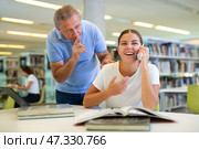 Elderly librarian asks young woman who is talking loudly on mobile phone to keep quiet. Стоковое фото, фотограф Яков Филимонов / Фотобанк Лори