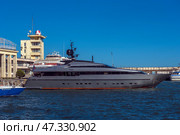 A fragment of the seaport in Yalta. In the center of the frame, an elegant and modern yacht called Orion is moored, painted dark gray with an orange line along the waterline. Nearby are boats and other vessels, and in the background are visible buildings of the port infrastructure, including the control tower with a characteristic dome. The sea is bright and rich blue, light ripples on the water indicate a fresh breeze. On the concrete wall behind is the inscription WELCOME, which emphasizes the tourist character of the place.The photo conveys the atmosphere of active marine life and the modern Yalta coast. (2021 год). Редакционное фото, фотограф Анна Кривицкая / Фотобанк Лори