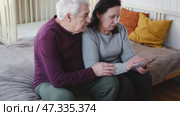 Old couple using a phone together while relaxing in the kitchen at home. Elderly man and woman spending leisure time browsing online with a smartphone. Happy senior married couple typing, learning. Стоковое видео, видеограф Марина Демидюк / Фотобанк Лори