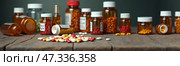 A collection of various prescription bottles and colorful pills is arranged on a rustic wooden surface, showcasing the diverse medications available. Wide Banner. Стоковое AI-изображение, AI-художник Sergey Grishin / Фотобанк Лори