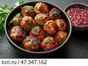Delicious meatballs, crisped to a golden crust, sprinkled with freshly chopped herbs (parsley). They are neatly laid out in a dark bowl. Next to them is a sauce based, probably cranberry or chili, with a characteristic texture and spice. The dish looks hearty, flavorful and perfect for serving at either lunch or dinner. Стоковое AI-изображение, AI-художник Анна Кривицкая / Фотобанк Лори