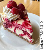 A delicious slice of raspberry cheesecake on a white plate. The base is shortcrust pastry, and the cake itself consists of a delicate creamy mass with bright raspberry veins. The top is decorated with fresh raspberries and caps of whipped cream. The contrast of white and rich berry shades gives the dessert visual expressiveness and emphasizes its freshness and sweetness. This delicacy seems to be created for a cozy tea party or a festive dessert. Стоковое AI-изображение, AI-художник Анна Кривицкая / Фотобанк Лори