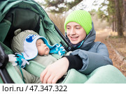 12-летний мальчик рядом со своим младшим братом-младенцем, который спит в зеленой коляске. в весеннем парке. фокус на подростке. Стоковое фото, фотограф Яна Проничева / Фотобанк Лори