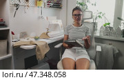 Entrepreneur in well-equipped sewing workshop recording video about growing her bespoke clothing brand. Speaking confidently on camera, she shares experiences, strategies handmade fashion business. Стоковое видео, видеограф Енваев Андрей / Фотобанк Лори